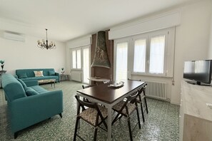 Uma sala de estar com sofá, mesa de jantar, cadeiras, lareira e televisão.