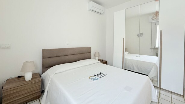 A hotel room with a bed, nightstand, lamp, air conditioning unit, and a large mirror. - B002 - Bellaria, large apartment close to the sea (Bellaria)