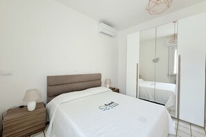 Quarto de hotel com cama, mesa de cabeceira, luminária, ar condicionado e um espelho grande.