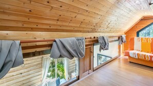 Eine Holzbalkendecke, ein Balkon mit grauen Vorhängen und ein orangefarbenes Sofa mit gemustertem Bezug.