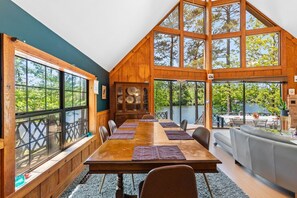 A large dining area with a long table, wooden walls, and large windows overlooking a lake.