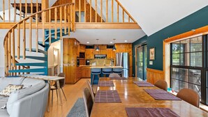 A spacious living area with a wooden staircase, a kitchen with modern appliances, and a dining area with a large window. - Riverfront Retreat with Dock, Kayaks and Views (Shelby)