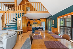 A spacious living area with a wooden staircase, a kitchen with modern appliances, and a dining area with a large window.