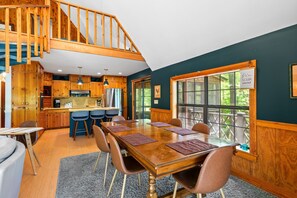 Une cuisine spacieuse avec des meubles de rangement en bois, un coin repas doté d’une grande table et de chaises, et un escalier menant à l’étage supérieur.