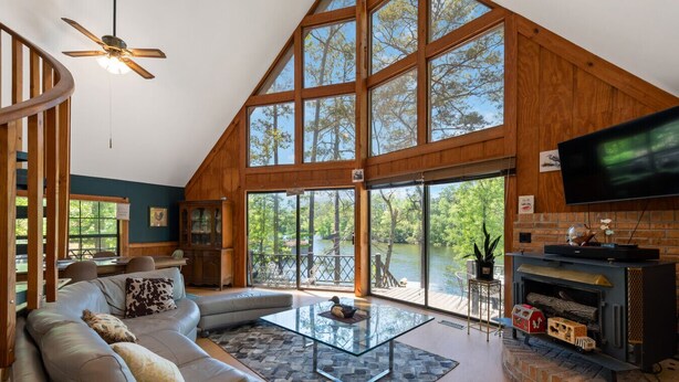 A spacious living room with a large window, a fireplace, and a ceiling fan. - Riverfront Retreat with Dock, Kayaks and Views (Shelby)