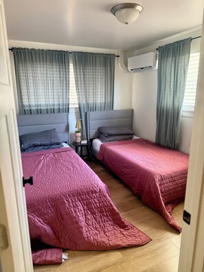 Et værelse med to senge, grå gardiner, en loftlampe og en aircondition.