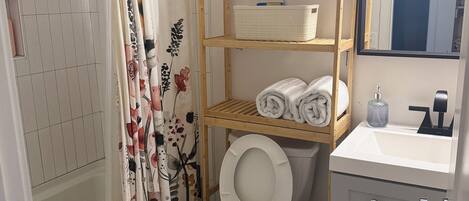 Kylpyhuone, jossa on suihku, wc ja puinen hylly, jossa on pyyhkeitä.