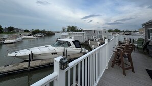 A marina with boats docked, a wooden deck with chairs, and a view of the water and buildings in the background.