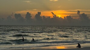 A sunset over the ocean with waves and silhouettes of people.