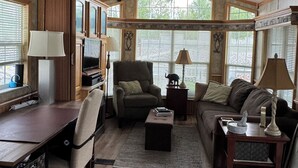 A spacious living room with a ceiling fan, wooden flooring, a desk with a computer, a sofa, and a coffee table.