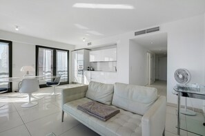 A modern living room with a sofa, a glass coffee table, and a fan. - Juan les Pins Seafront – 2-Bedroom Bay Side Apartment (Antibes)