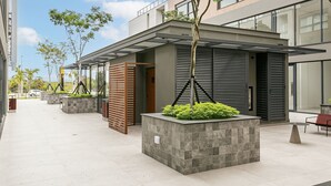 A modern building with a covered outdoor area, planters with greenery, and a seating area. - SC-401 | Tech Hub | Gym #SG08 (Florianópolis)