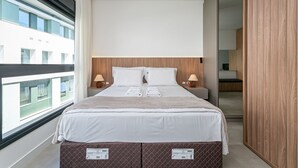 A modern hotel room with a large bed, two bedside lamps, a view through a window, and a wooden wardrobe. - SC-401 | Tech Hub | Gym #SG08 (Florianópolis)
