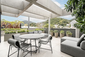 A modern outdoor patio with a round table and chairs, a grey sofa, and potted plants.