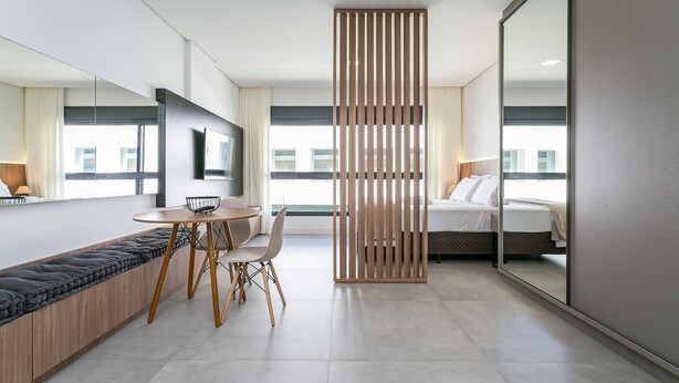 A modern hotel room with a sofa, dining table, chairs, a bed, a large mirror, and a view of the city. - SC-401 | Tech Hub | Gym #SG08 (Florianópolis)