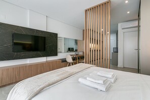 A modern hotel room with a large bed, a TV mounted on the wall, a wooden desk, and a separate bathroom.