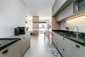 A modern kitchen with a black countertop, stainless steel appliances, and a wooden partition.