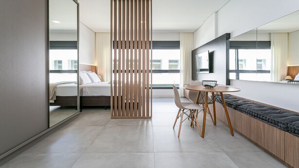 Et moderne hotelværelse med seng, spiseplads, et stort spejl og udsigt over byen.
