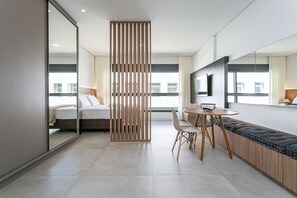 Une chambre d’hôtel moderne équipée d’un lit, d’un coin repas, d’un grand miroir et offrant une vue sur la ville.