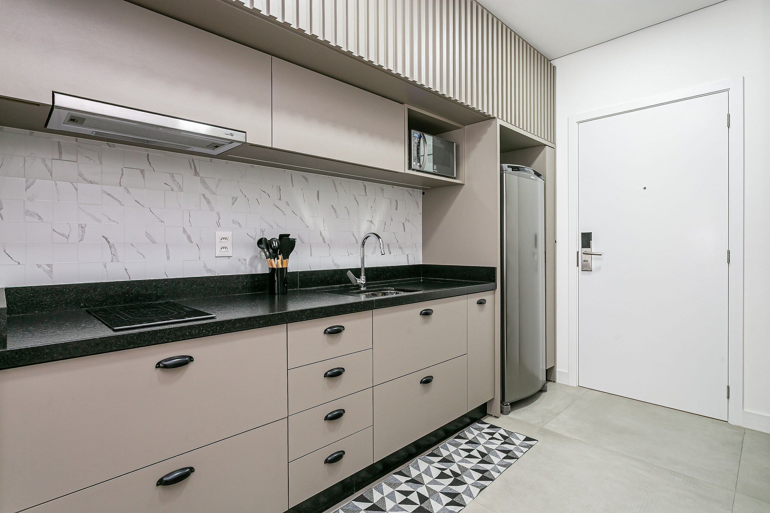 A modern kitchen with a black countertop, white cabinets, and a stainless steel refrigerator.