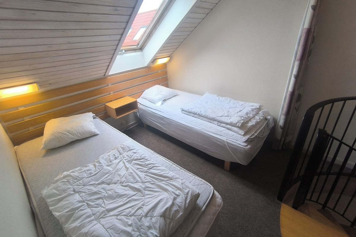 A small, compact room with two beds, a skylight, and a wooden headboard.