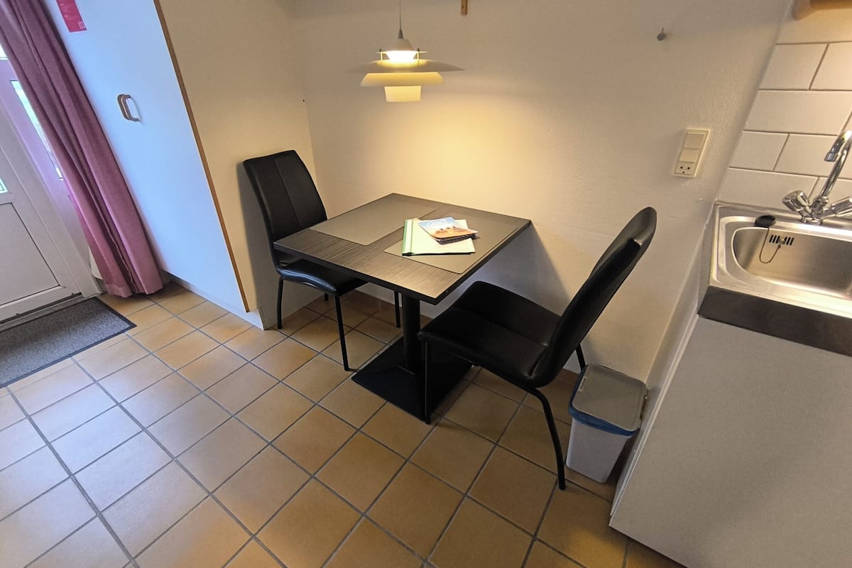 A small kitchen with a dining table, chairs, a sink, and a hanging light fixture.