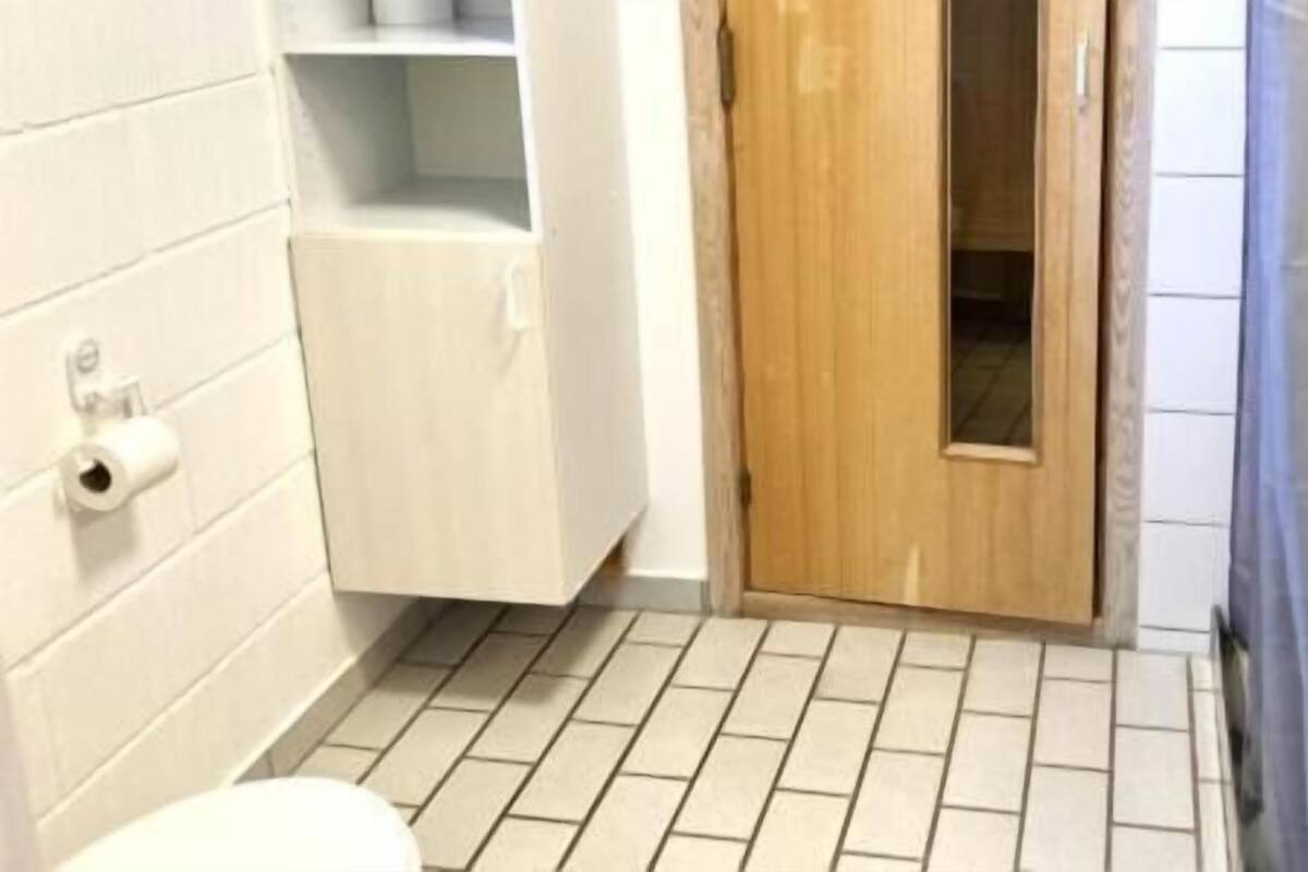A bathroom with a toilet, a wooden door, and a shower area.
