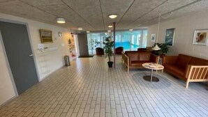 Een ruime lobby met een betegelde vloer, een receptiebalie, een bruine leren bank en een potplant.