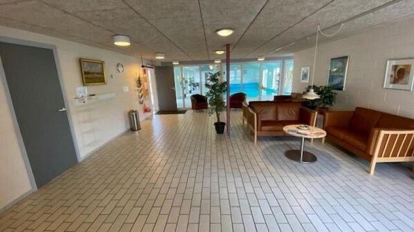 A spacious lobby with a tiled floor, a reception desk, a brown leather sofa, and a potted plant.