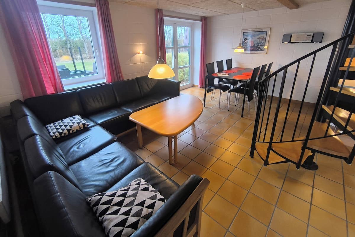 A furnished living area with a sofa, table, chairs, a staircase, and a window with curtains.