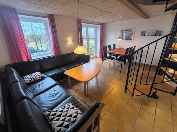 A furnished living area with a sofa, table, chairs, a staircase, and a window with curtains.