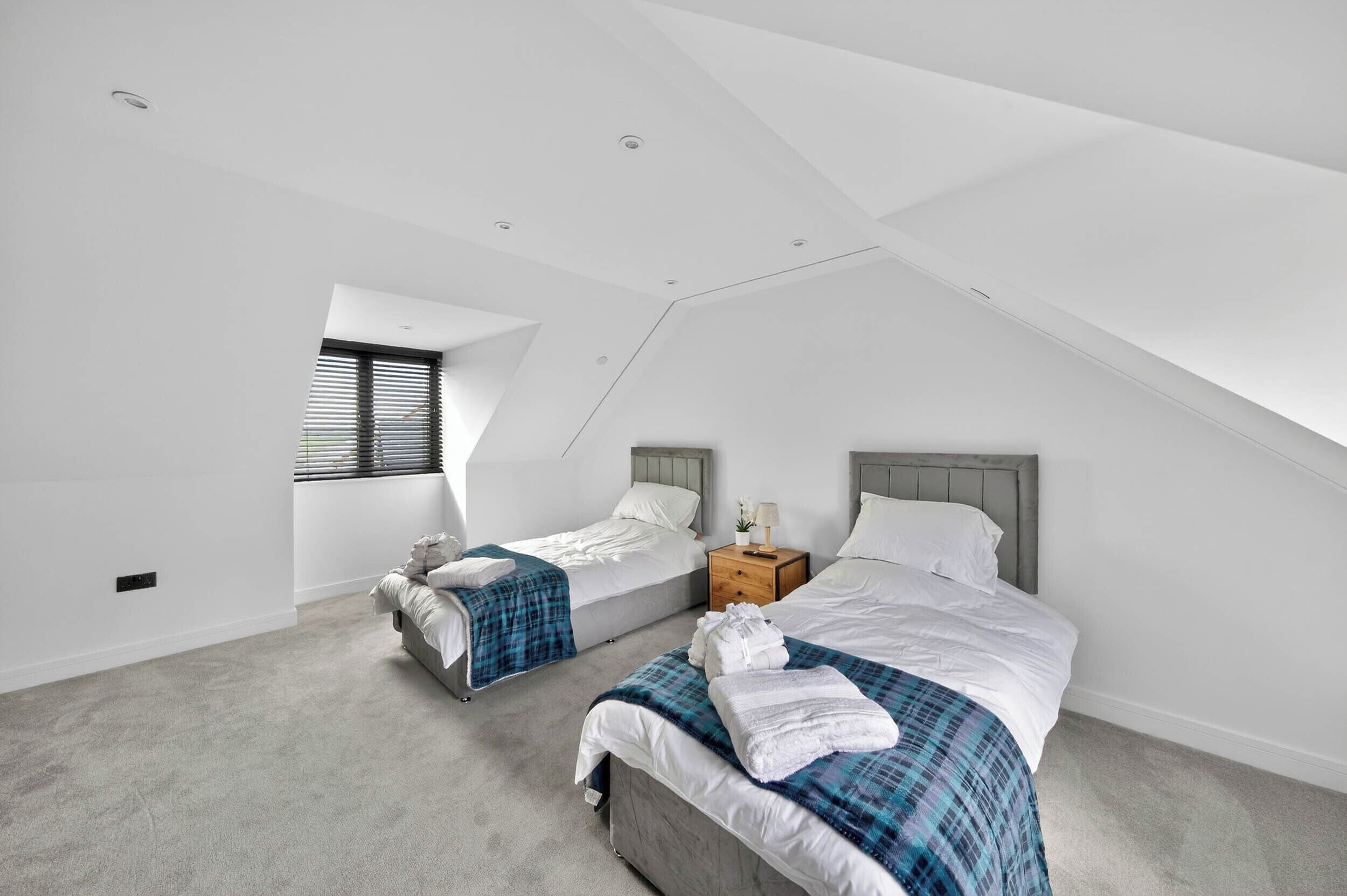 A modern bedroom with two beds, a skylight, and a small bedside table with a lamp.
