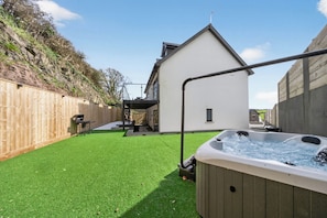 Un jardín con césped artificial, un jacuzzi, una valla de madera y una casa moderna.