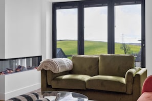 Una sala de estar con un sofá verde, una mesa de vidrio y vistas a un campo verde a través de amplios ventanales.
