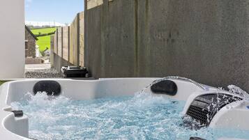 A hot tub with water splashing, a stone wall, and a view of a green field.