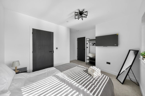Un dormitorio moderno con cama, mesita de noche, lámpara y televisor montado en la pared.