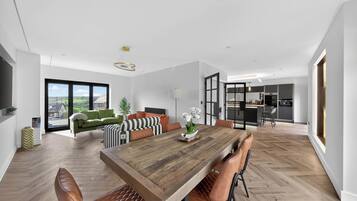 Una sala moderna con una mesa de comedor de madera, sillas de cuero, un sofá verde y vistas a través de amplios ventanales.