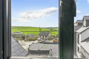 A view from a window overlooking a rural landscape with houses, a green field, and a clear sky. - Heddfan (Carmarthen)