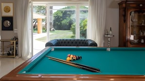Ein Billardtisch mit Kugeln, eine Couch und ein Schrank mit Gläsern.