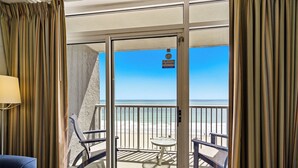Una habitación con puerta corrediza de vidrio que da a un balcón con vista a la playa.