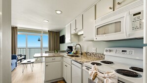 Una cocina moderna con microondas, estufa y lavaplatos, un comedor con mesa y sillas, y un balcón con vistas.