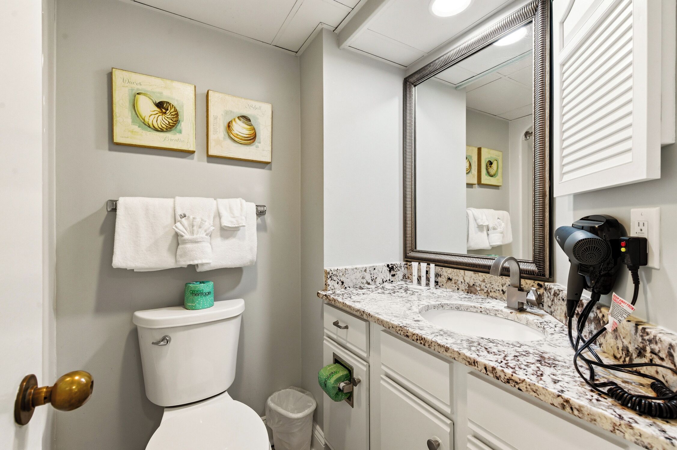 A bathroom with a toilet, sink, and mirror. There are towels hanging on the wall and a hairdryer on the counter.