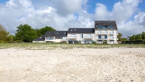 Un hôtel en bord de mer composé de plusieurs bâtiments, doté de balcons et offrant une vue sur une plage de sable au premier plan.