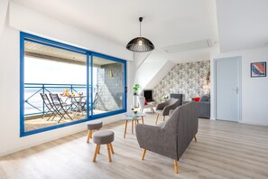 Ein modernes Wohnzimmer mit großem Fenster, einem Essbereich und einer Treppe, die in ein Obergeschoss führt.