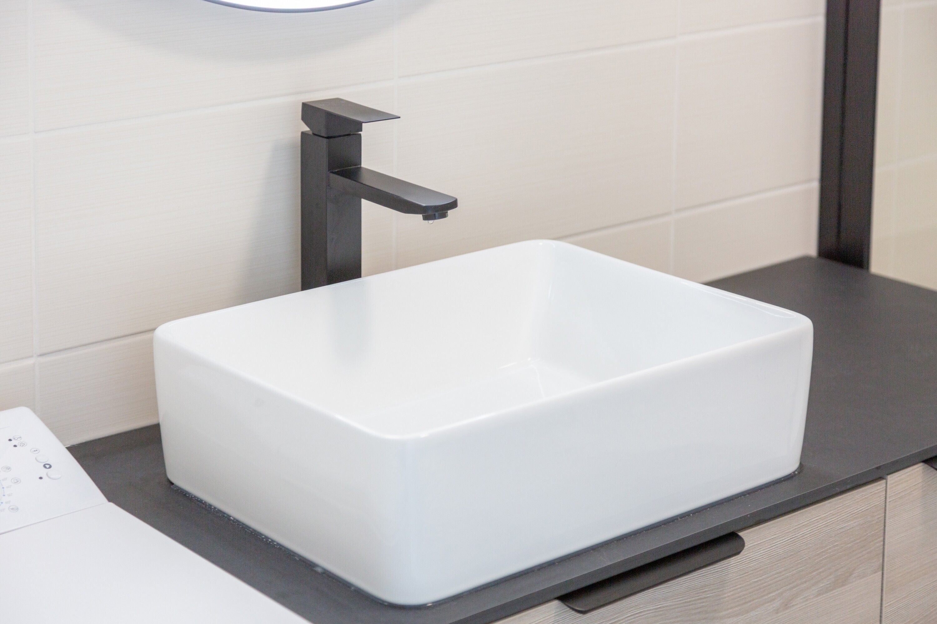 A modern bathroom with a white rectangular sink, a black faucet, and a wooden cabinet below.
