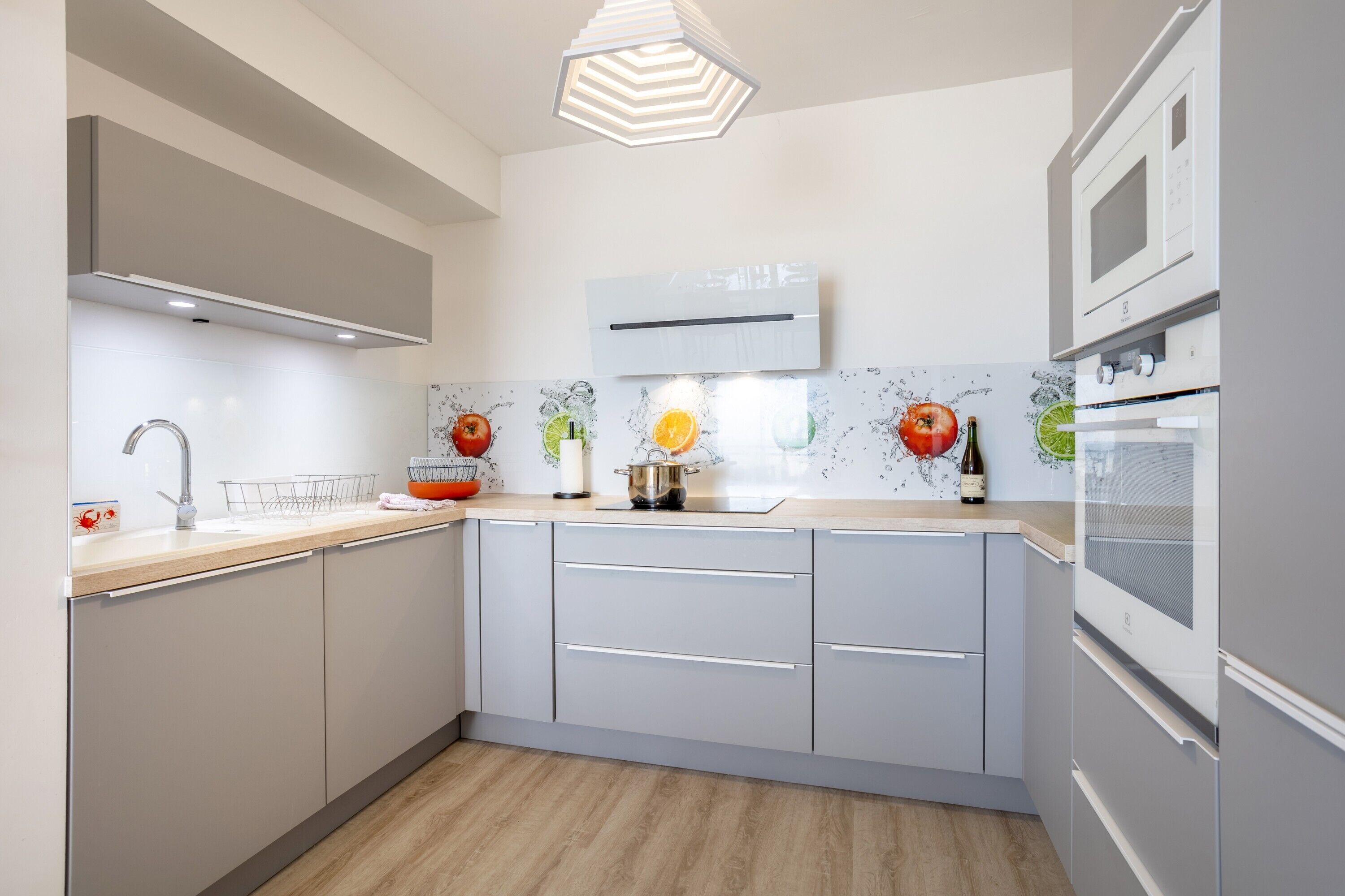 Una cocina moderna con armarios grises, encimera de madera, microondas, horno y un salpicadero decorativo.