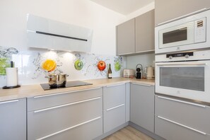Uma cozinha moderna com armários cinza, micro-ondas, forno e painel de fundo com desenhos de frutas.
