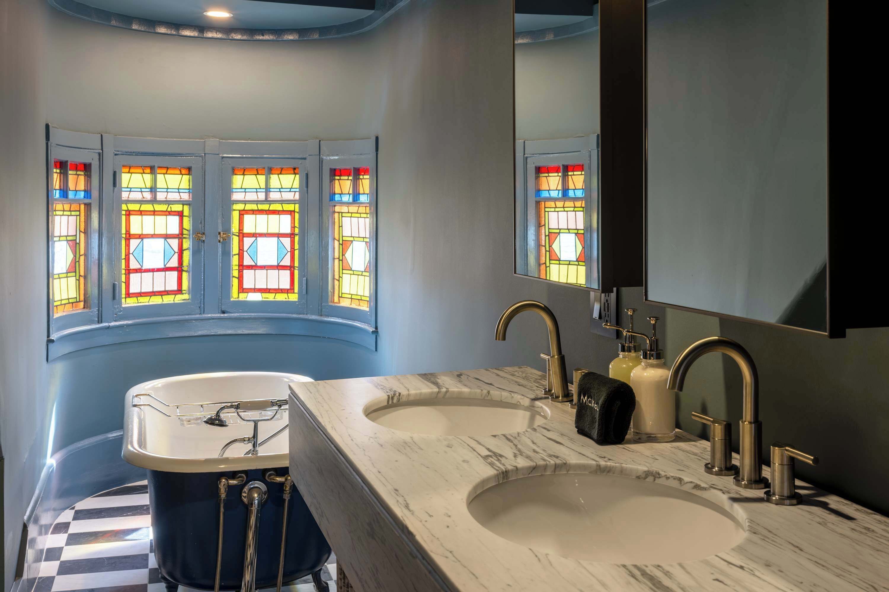 Une salle de bain avec deux lavabos, une baignoire et des vitraux.