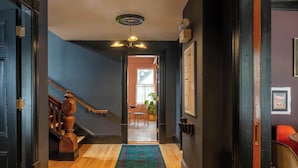Un pasillo con una escalera de madera, alfombra estampada y una lámpara en el techo.