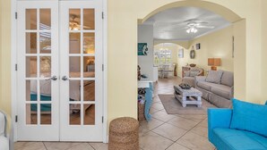 A living room with a blue sofa, a coffee table, and a dining area with a table and chairs. - Barefoot Beach Resort E206 - Liquid Obsession (Indian Shores)